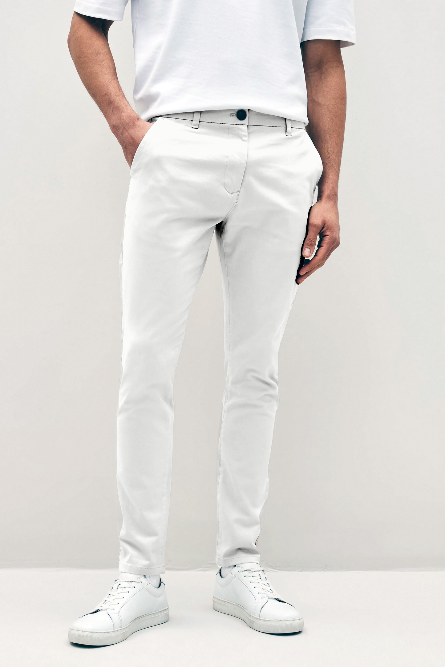 Mens white chinos with front slanted pockets, jetted back pockets. zip fly fastening and brown horne buttons on the waistband and back pockets, the fit is a slim fit, this is worn with a white tee and white unbranded trainers